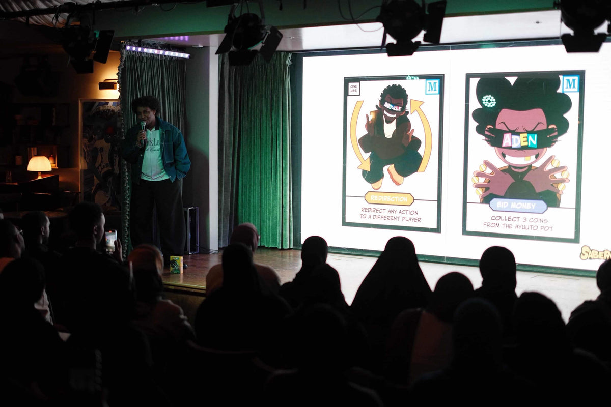 Saber Aidarus on stage, DULMI cards projected behind him, a full room watching.
