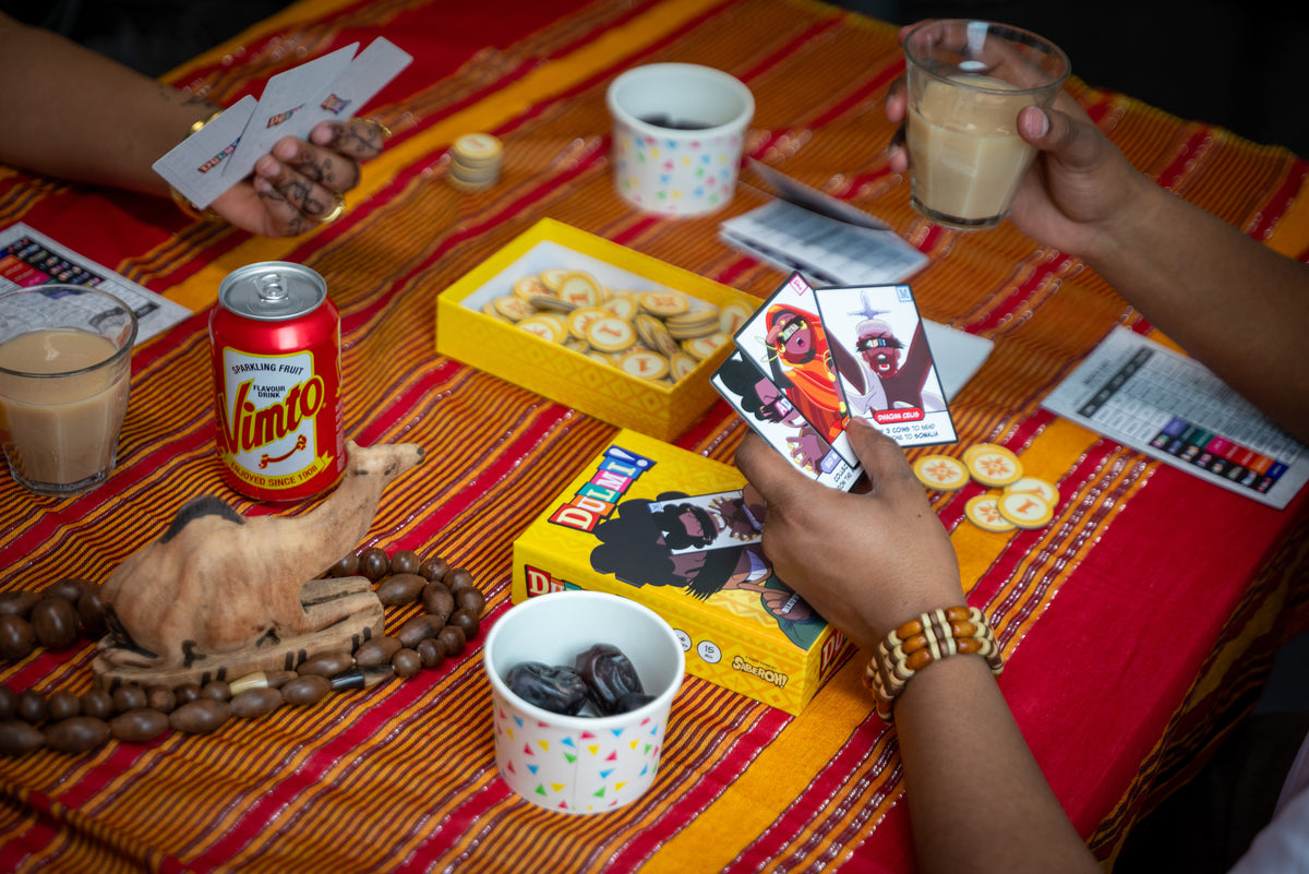 A DULMI game in progress: cards dealt across a table, tea and snacks between the players.